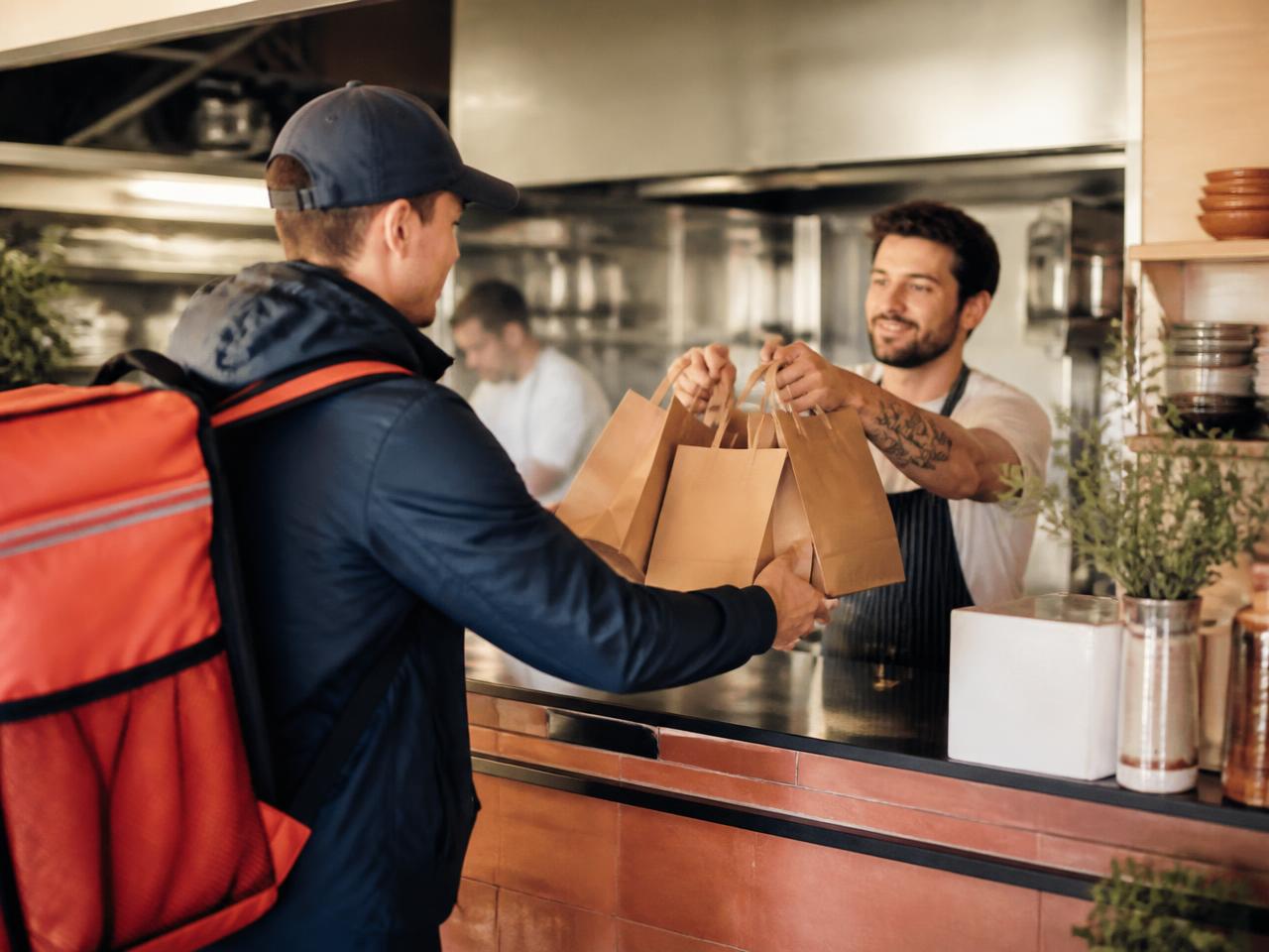 Fahrer nimmt Tüten mit Essen an der Ausgabe eines Restaurants entgegen